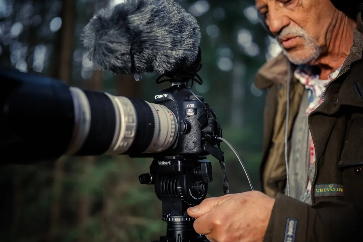 Older man filming wildlife with a microphone-fitted camera on a tripod