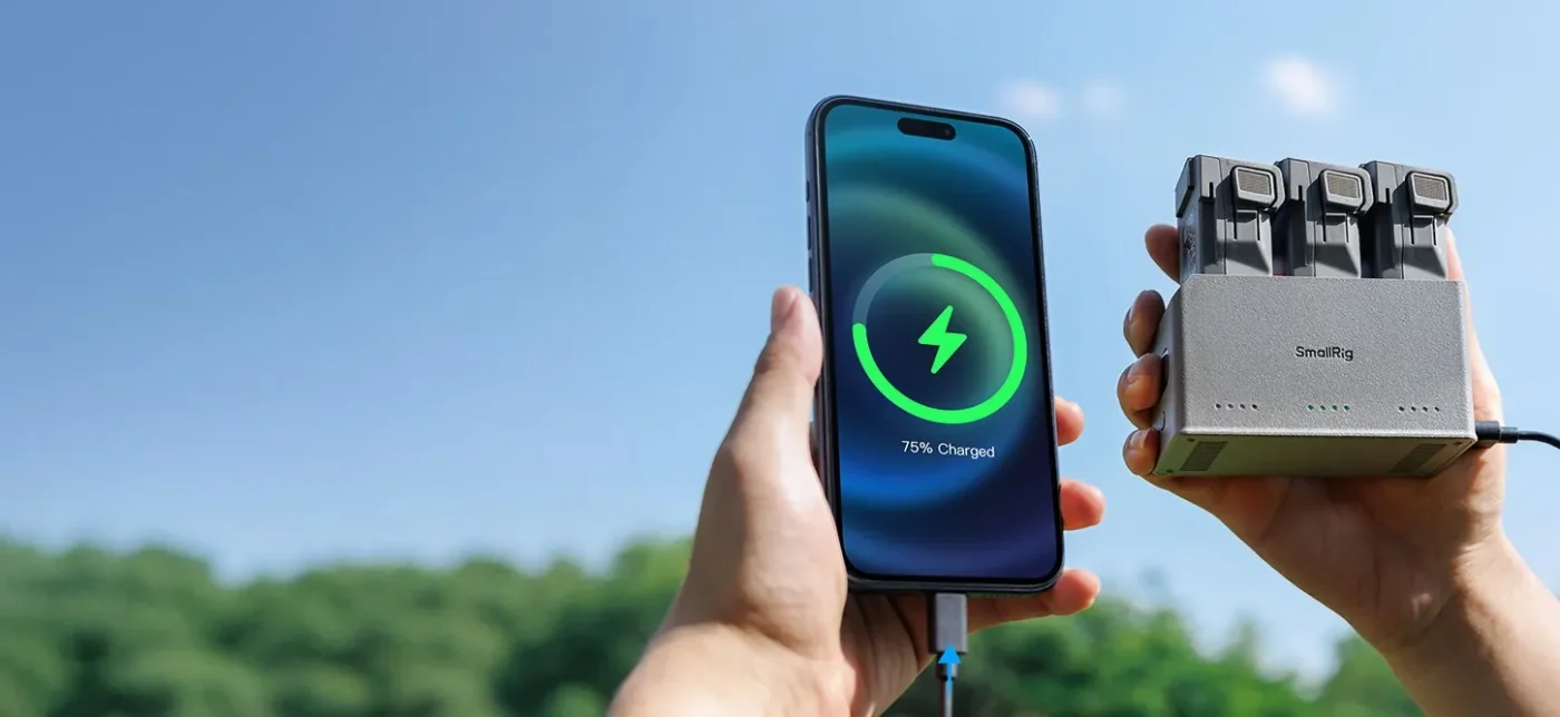 A hand holding a phone charging from a charger outdoors