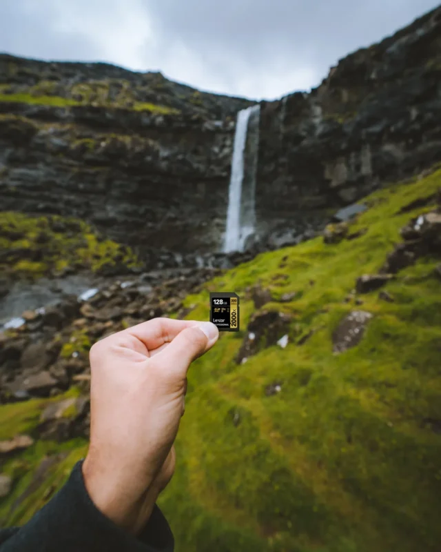 A hand holding up a memory card in front of a waterfall