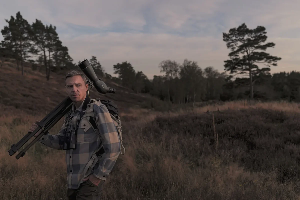 Birder with a spotting scope on a tripod on a heath at dusk