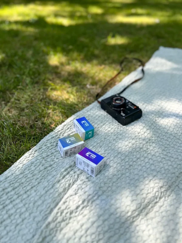 Film boxes and a camera on a picnic blanket in the grass