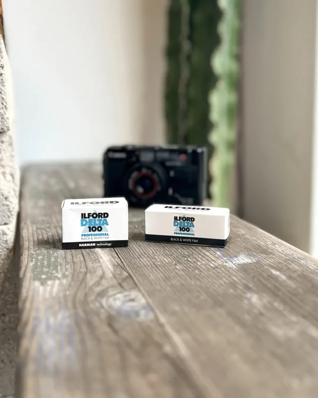 Boxes of black and white film next to a camera on a weathered wooden table