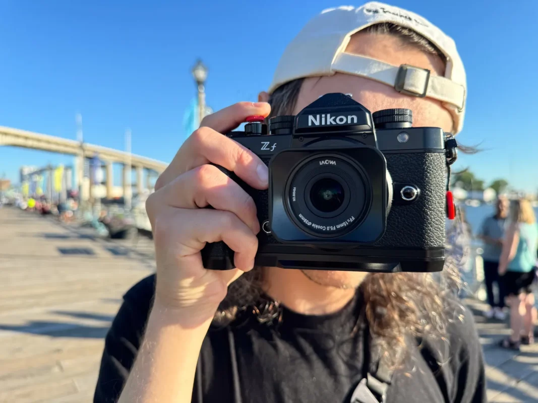 Photographer in a cap pointing a wide-angle lens straight at the viewer