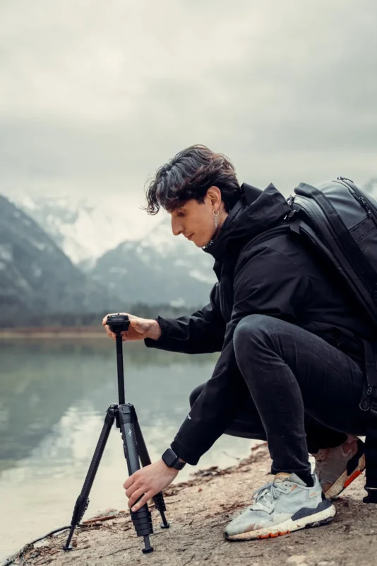 Photographer crouching to set up a tripod by a misty lake