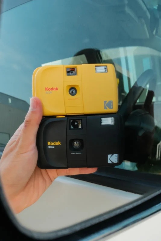 Hand holding a yellow Kodak film camera by a window