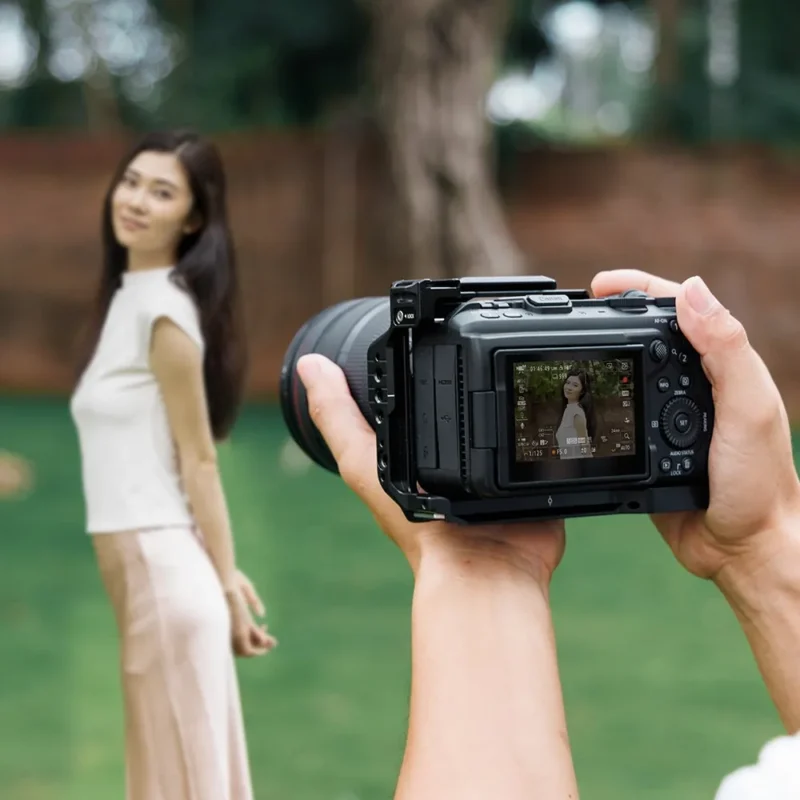 Hands hold a caged camera framing a woman in a garden