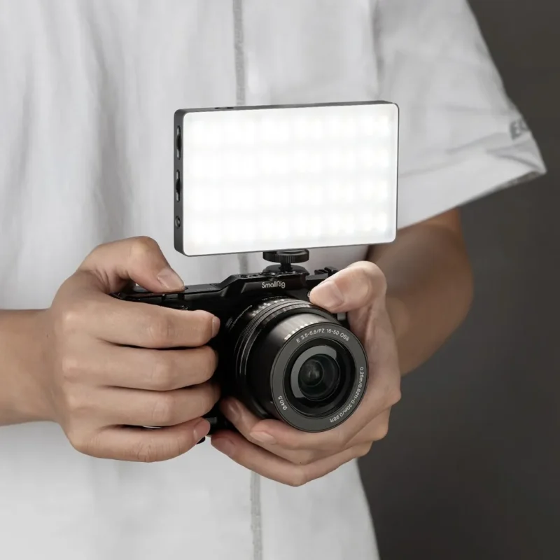 Hands holding a camera with a small LED panel mounted on top