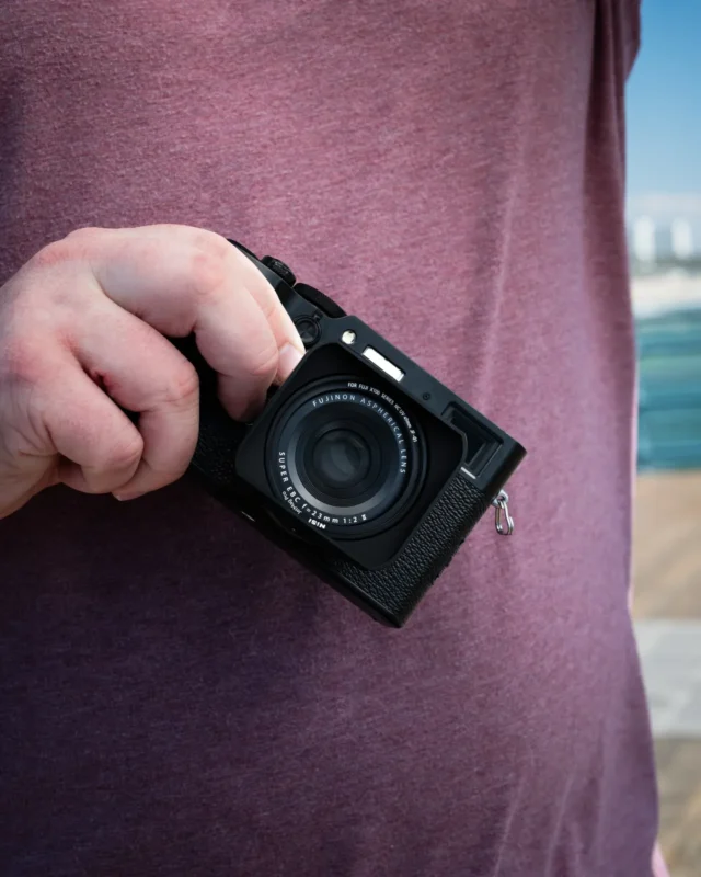 Hands holding a compact camera with a hood on the lens