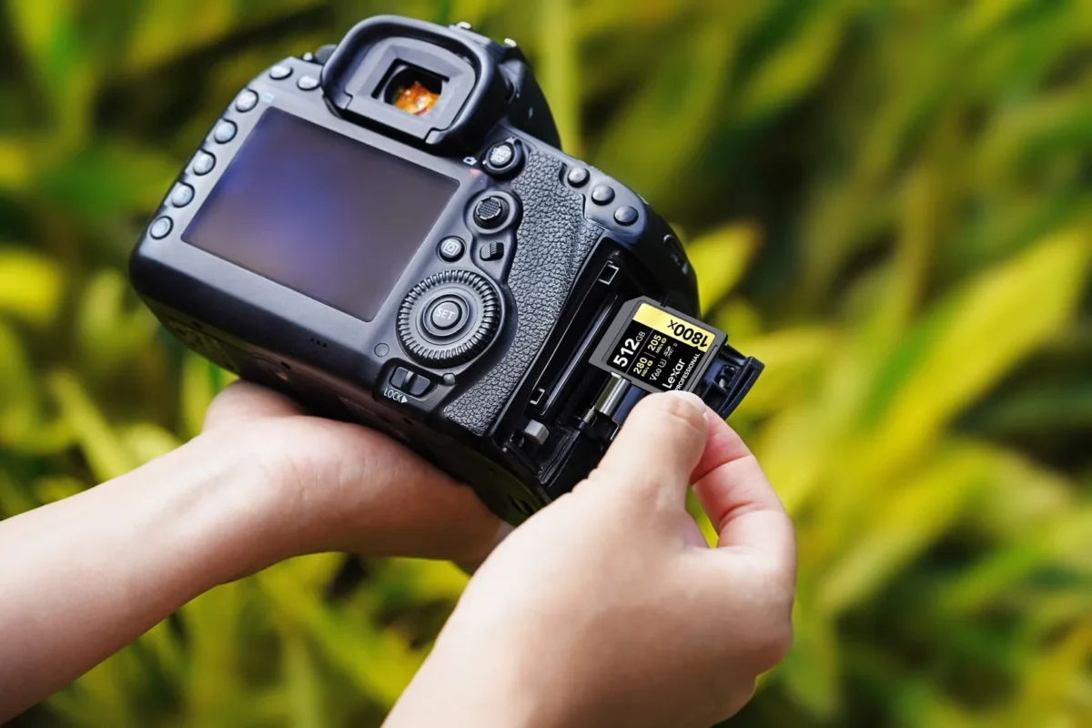 Hands loading a memory card into a DSLR outdoors on the grass