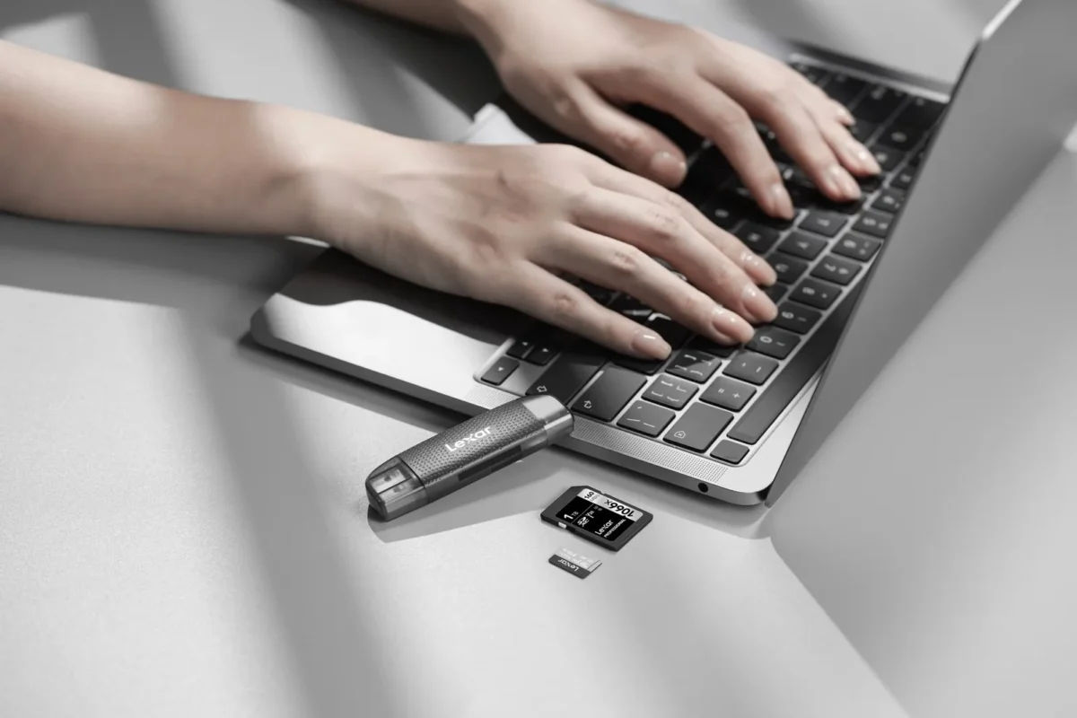Hands typing on a laptop with a card reader plugged in