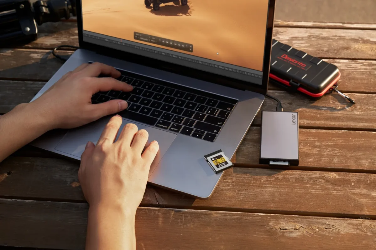 Hands typing on a laptop with an SSD and a memory card beside it