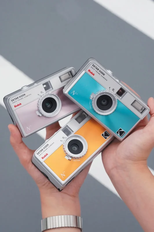 Hands holding three pastel half-frame film cameras
