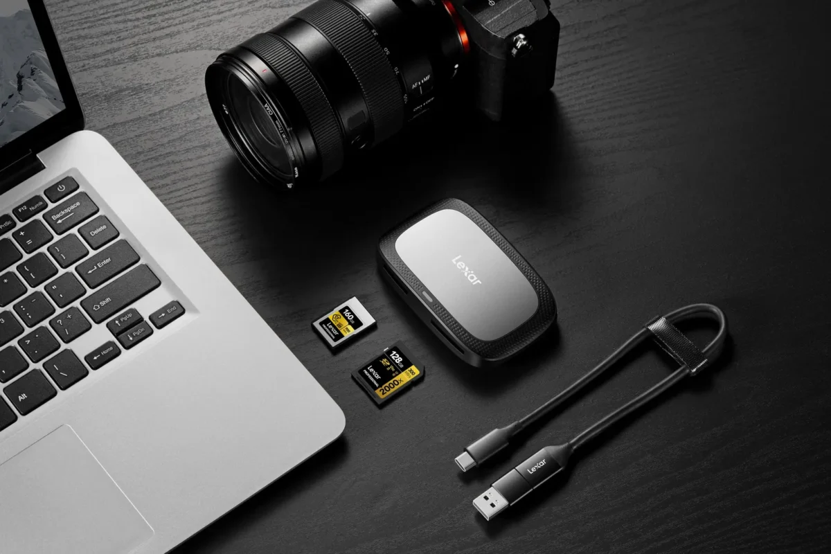 Camera, memory cards and card reader beside a laptop on a dark desk