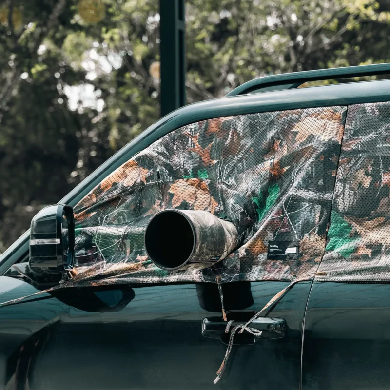 Camouflage curtain in a car window with a lens poking out