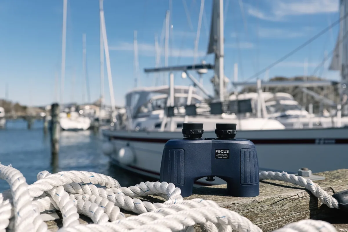 Binoculars on a jetty with sailing boats in the harbour behind