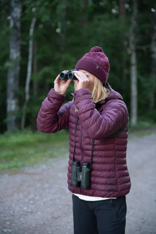 Woman in a beanie watching birds in the forest with binoculars