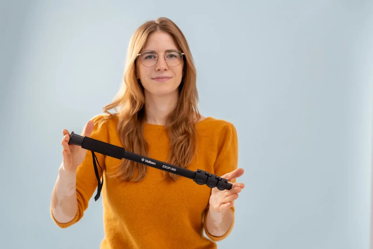 Woman in an orange sweater holding up a folded monopod
