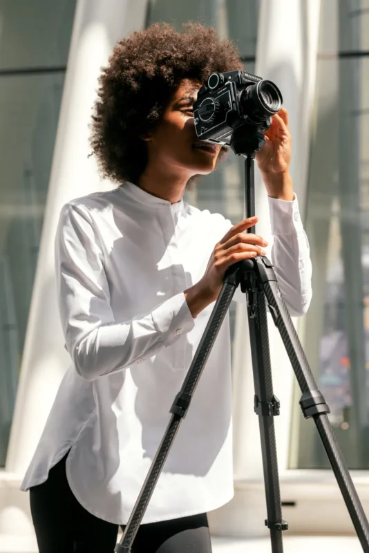 Woman in white adjusting a tall tripod outdoors