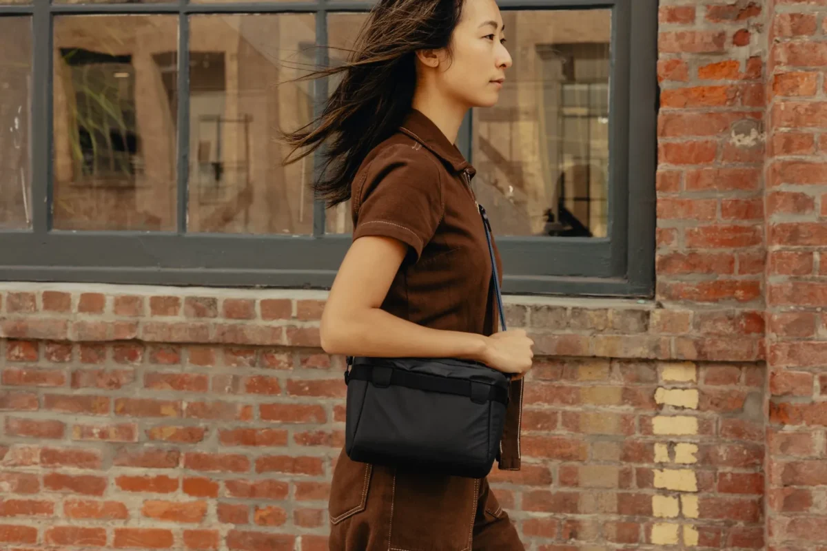 Woman with a sling bag walking past a brick wall