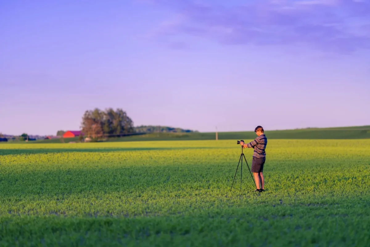 Woman with a tripod in a green field in evening light