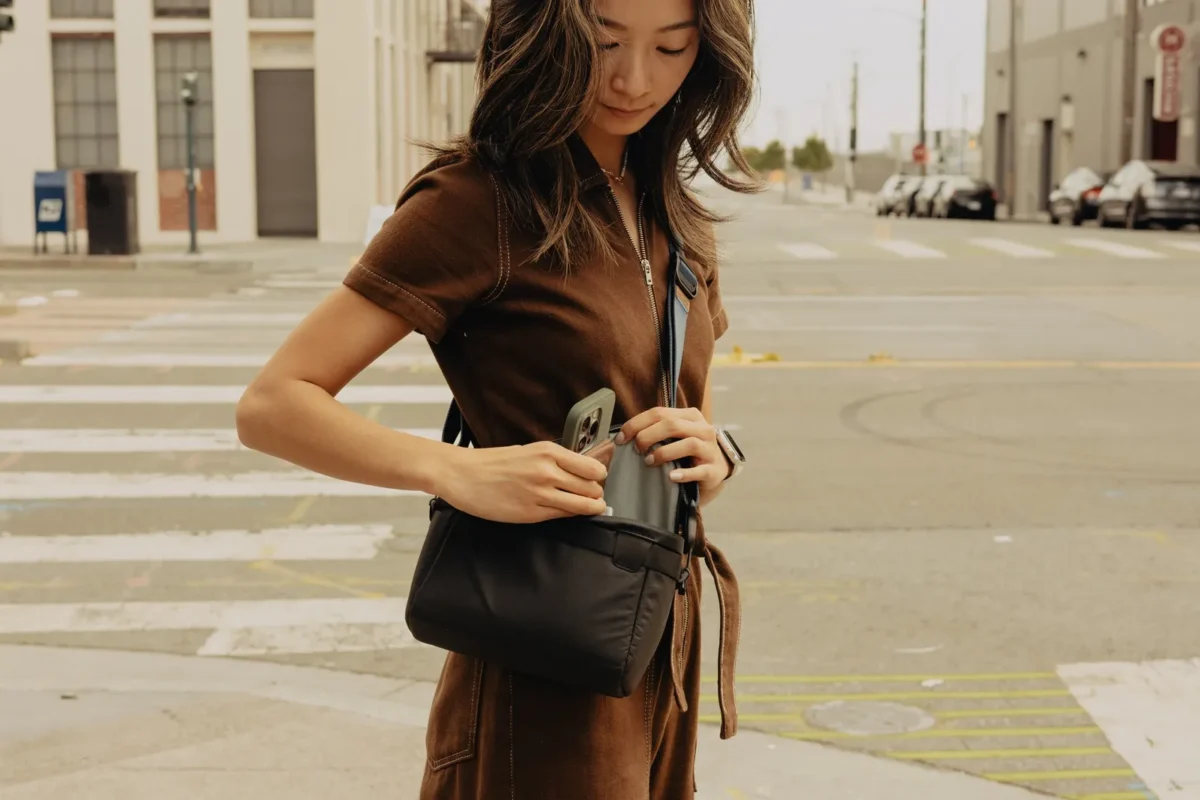 Woman on a city street reaching into her sling bag