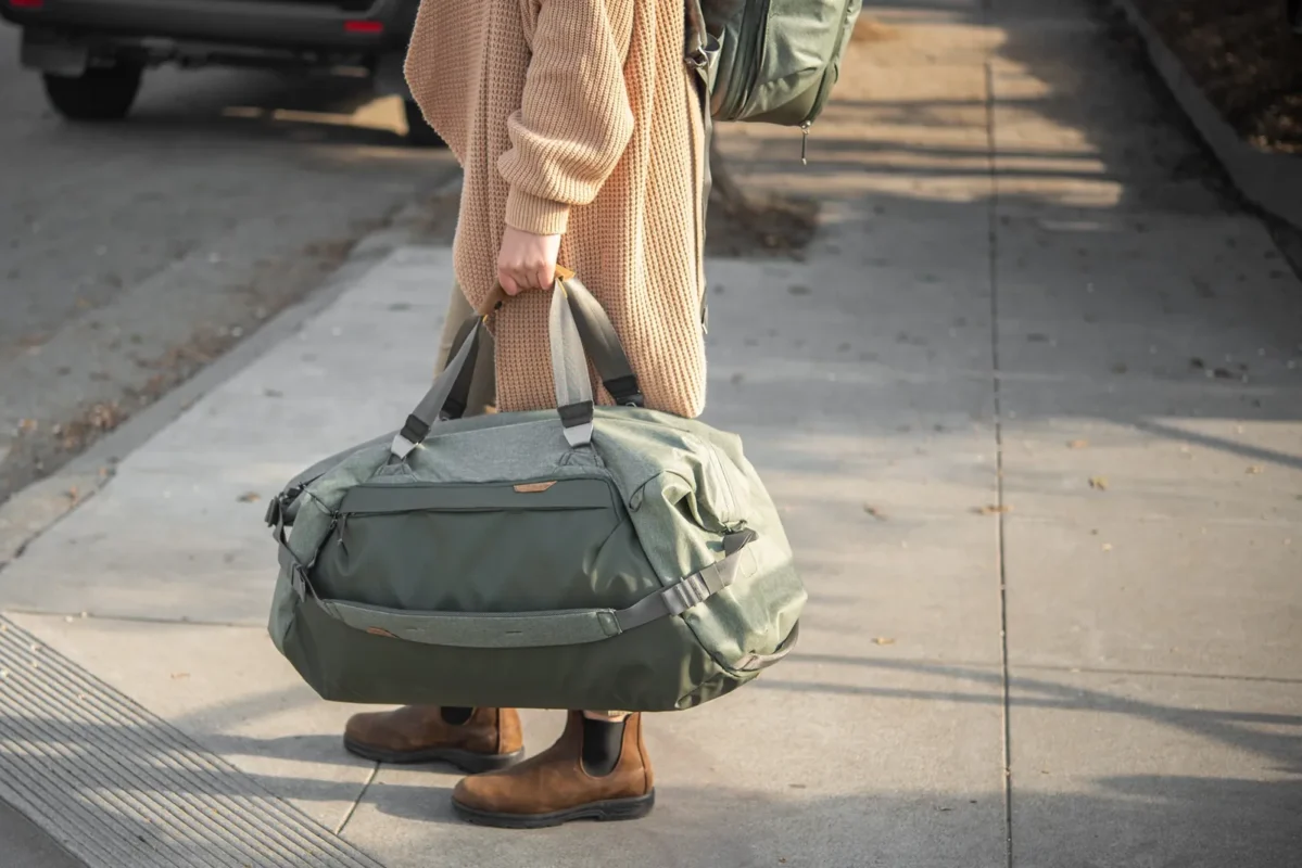 Woman carrying a green duffel bag along a sunny street