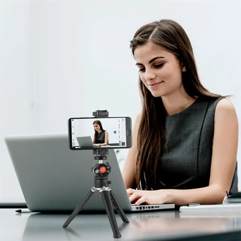 Woman at a laptop with her phone on a small tabletop tripod