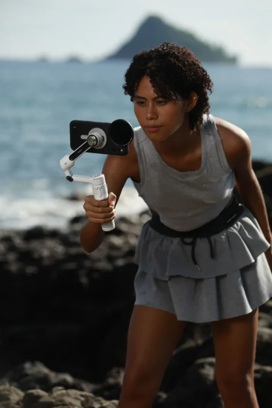 Woman by the sea leaning in with a phone rig in her hands