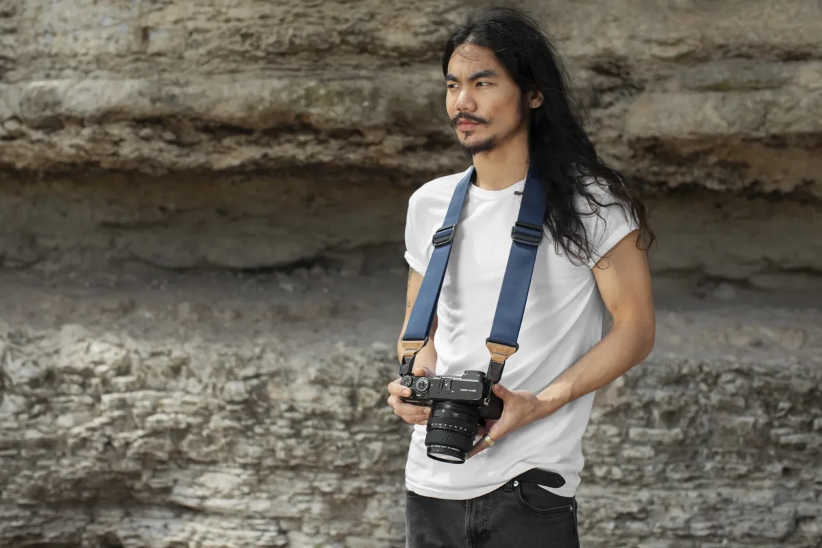 Long-haired photographer with a camera strap by a cliff