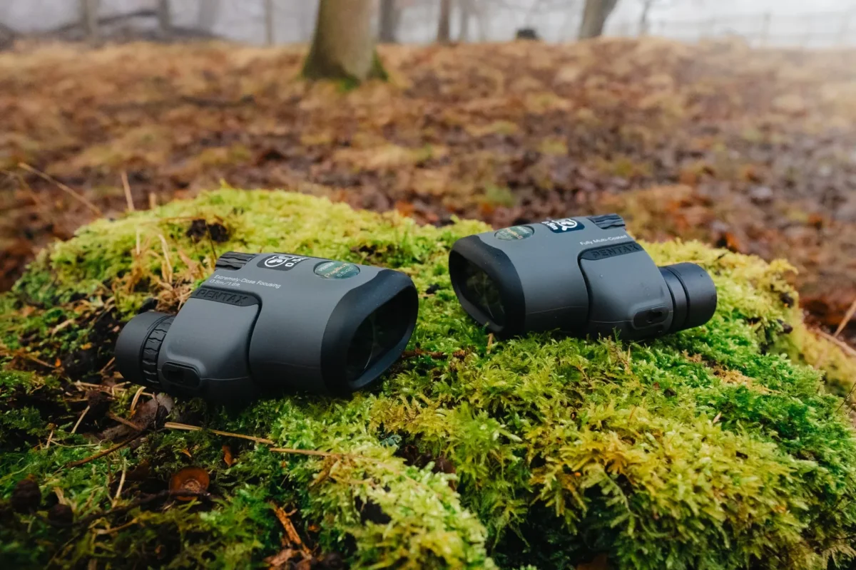 Small binoculars and their case on green moss