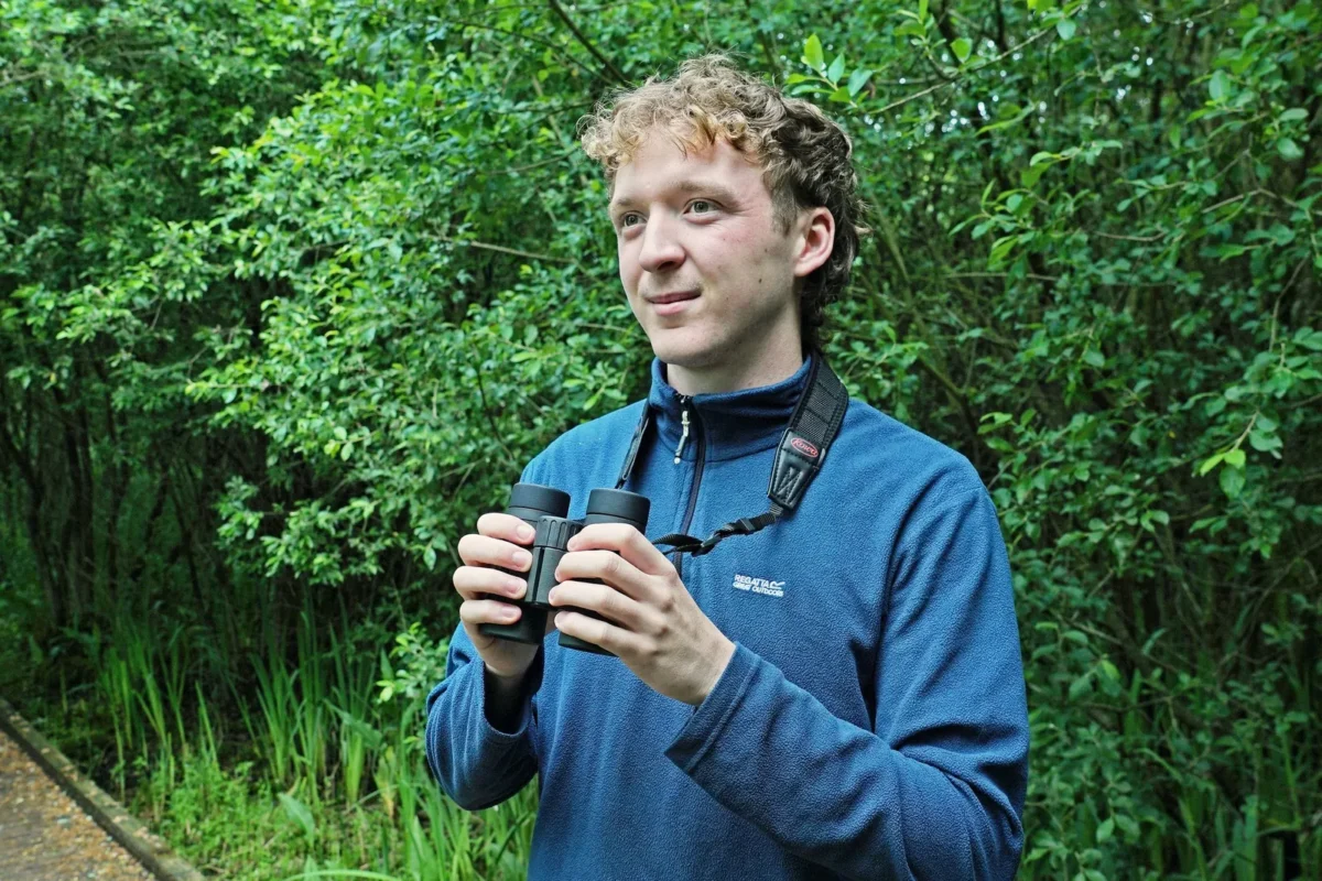 Man in a blue fleece with binoculars among trees