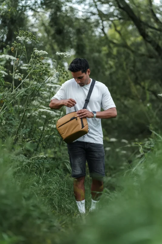 Man in a garden reaching into a beige sling bag