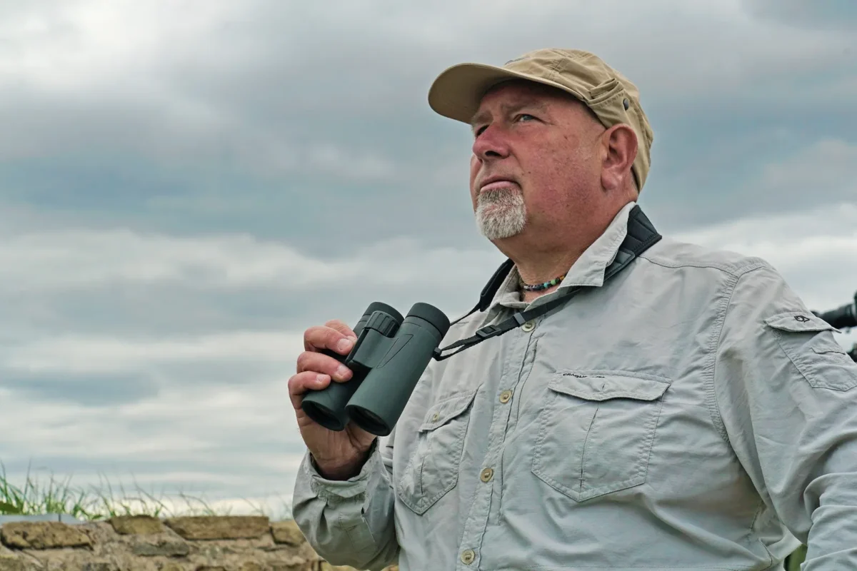 Man in a cap using binoculars on a windy coast
