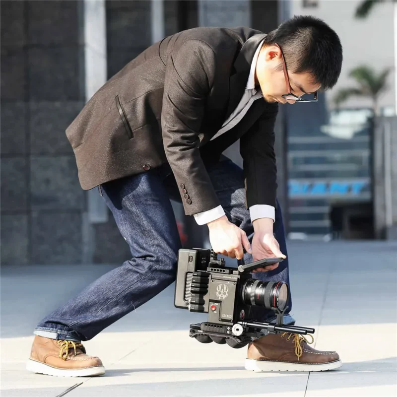 Man in a suit crouches with a shoulder-rigged camera