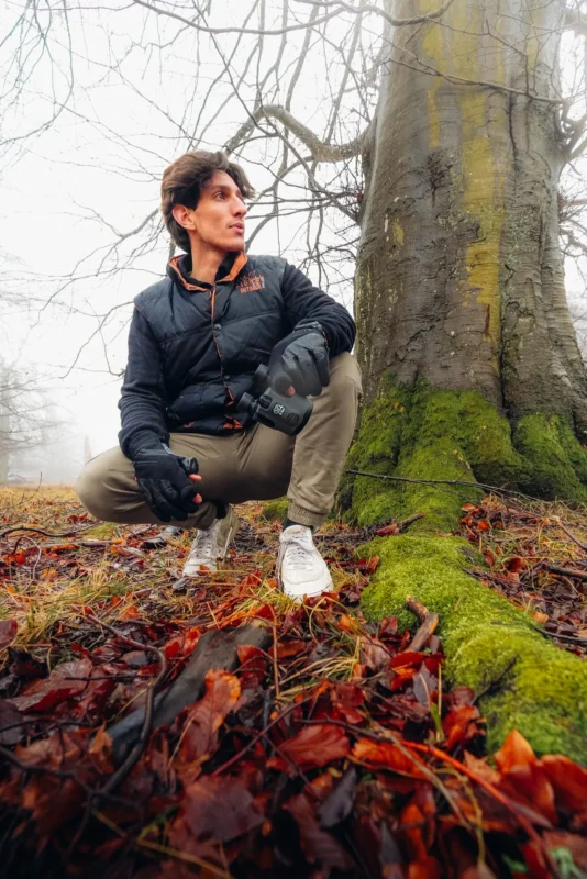 Man kneeling on mossy ground with compact binoculars