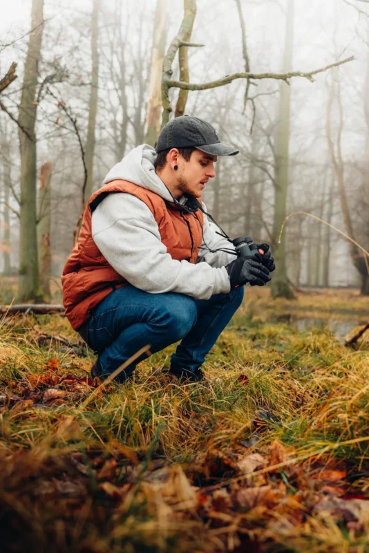 Man crouching in an autumn forest with binoculars