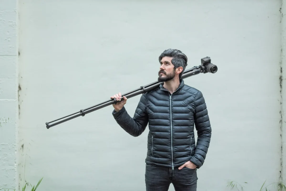 Man carrying a folded tripod over his shoulder in the hills