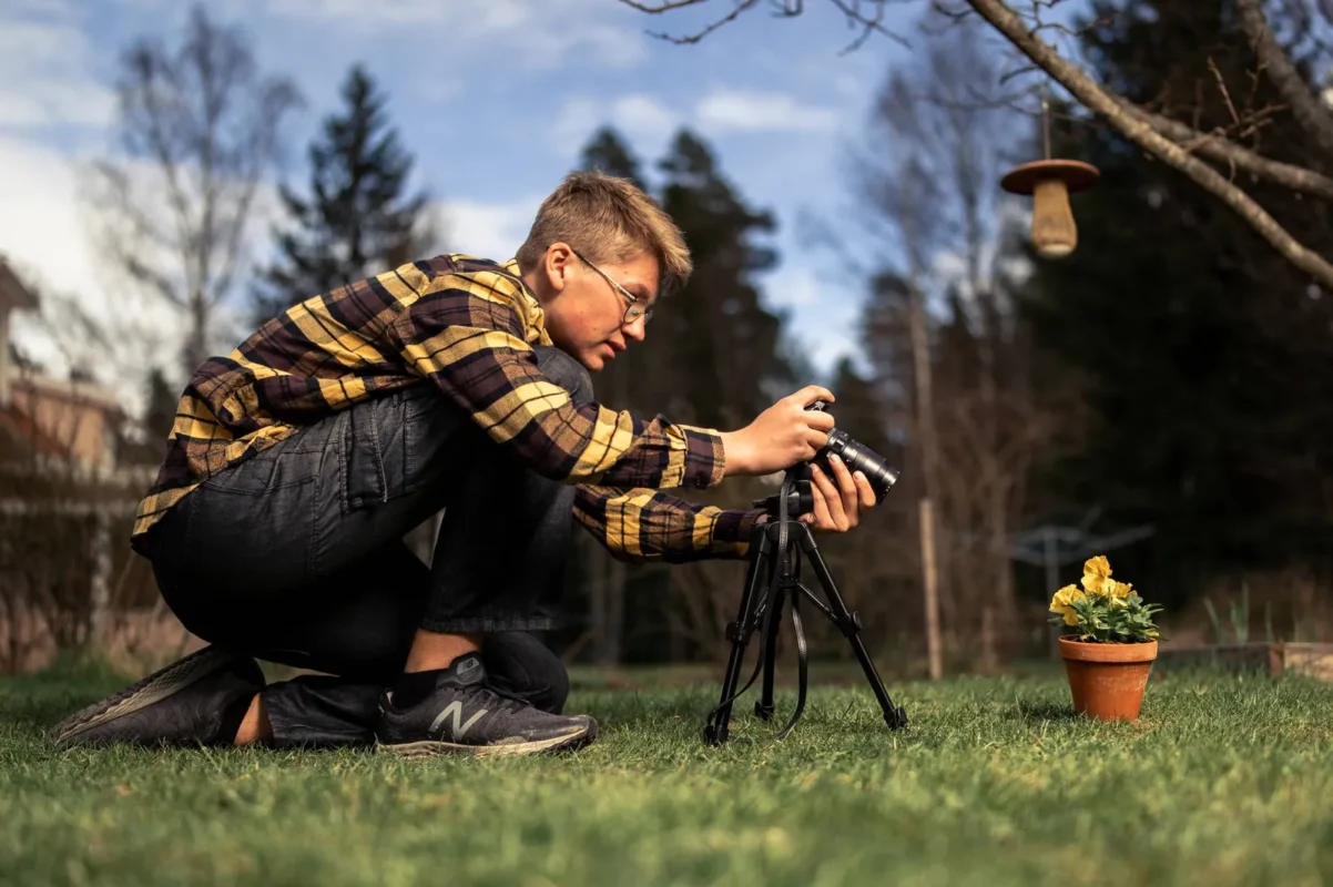 Man kneeling to frame a shot with the camera on a tripod in the woods
