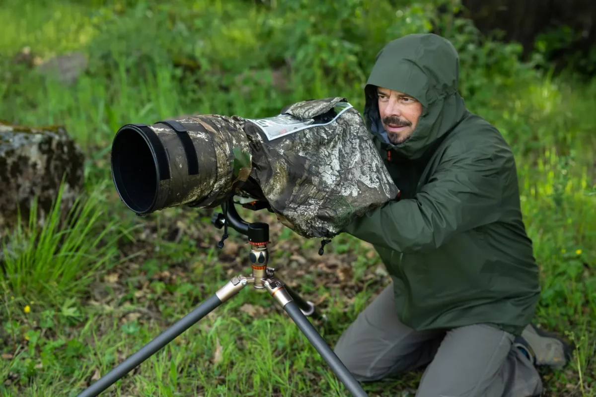 Wildlife photographer in rain gear with a covered telephoto lens