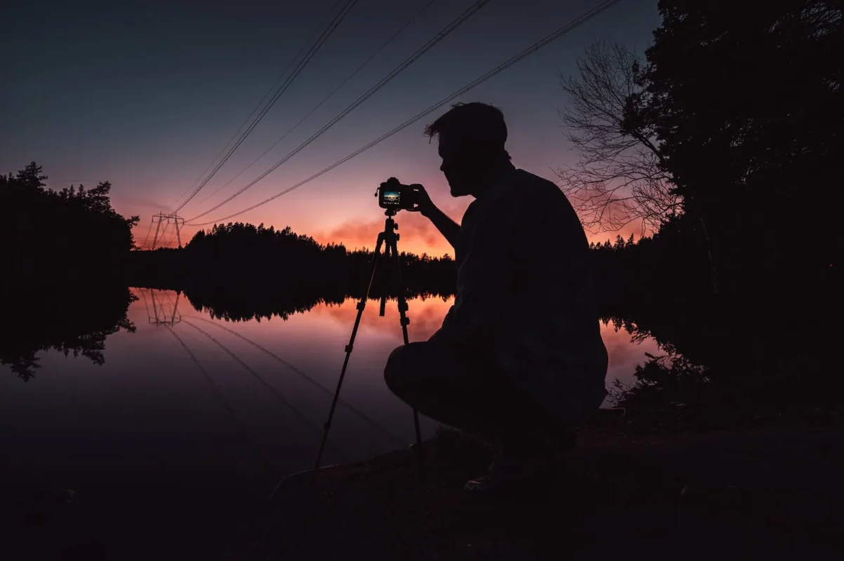 Silhouette of a photographer with a tripod by a lake at sunset