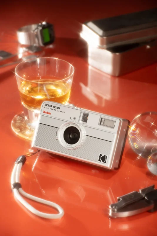 Silver striped Kodak film camera on an orange table next to a drink