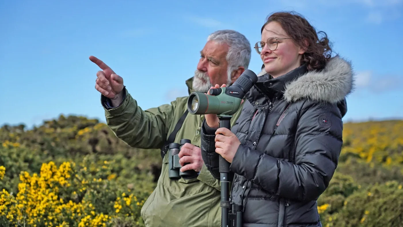 Two birders looking through a spotting scope on a tripod outdoors
