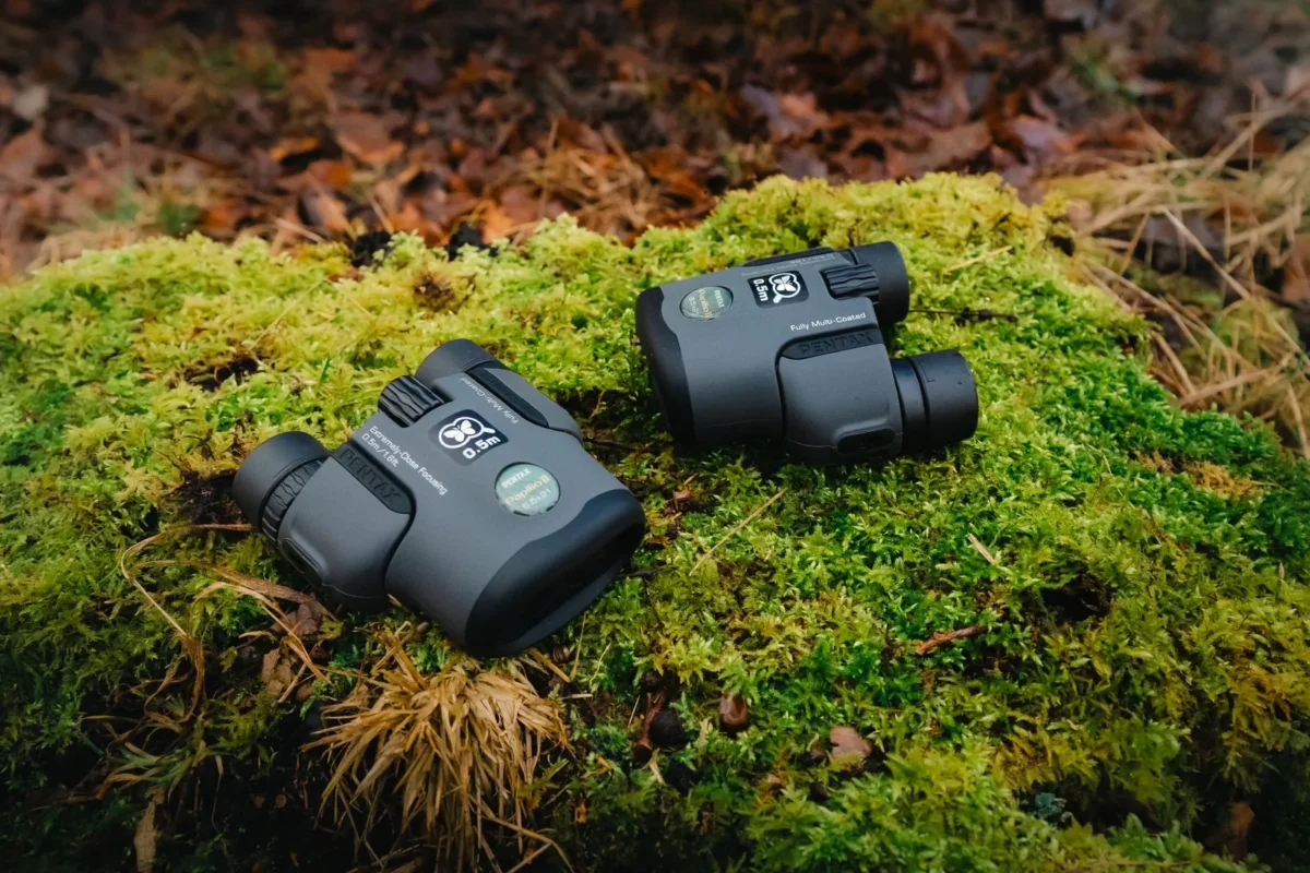 Two small binoculars resting on moss