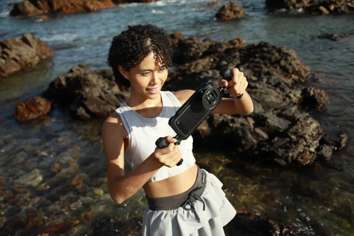 Young woman filming with a phone rig from the rocks by the sea