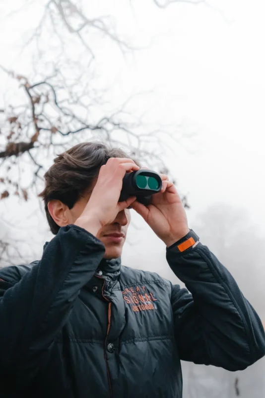 Young man scanning a misty forest with binoculars