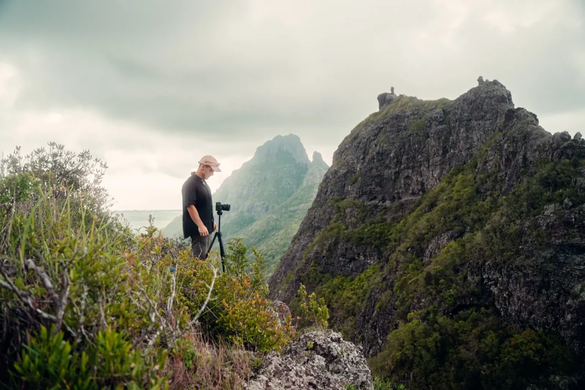 Hiker with a tripod on a green mountain ridge